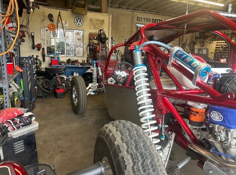 Red custom car with oversized shocks and suspension parts in automotive workshop with VW sign and other vehicles