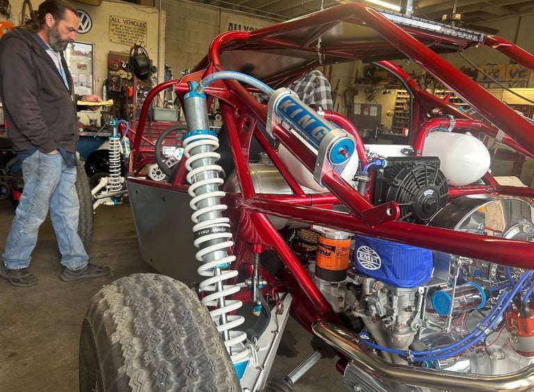 Red custom drag racing vehicle with exposed engine and blue nitrous bottles in garage workshop with man observing