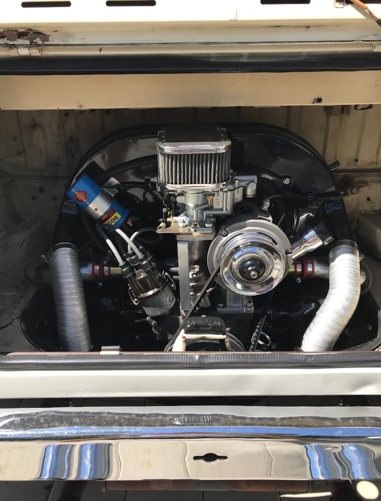 Custom car engine with polished chrome air filter, intake manifold, and dual white exhaust tubes mounted in engine bay