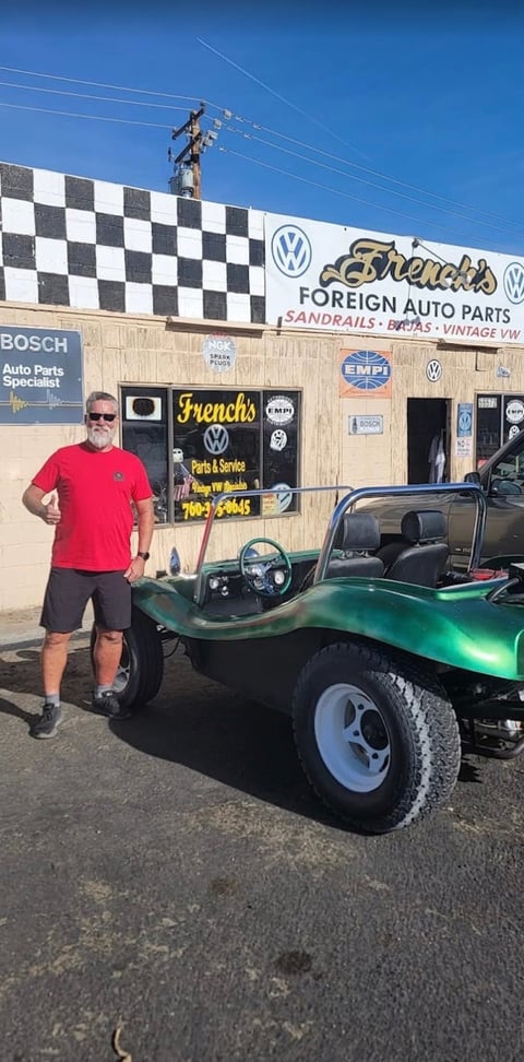Man standing next to green custom dune buggy outside Frenchs Foreign Auto Parts shop with checkered banner