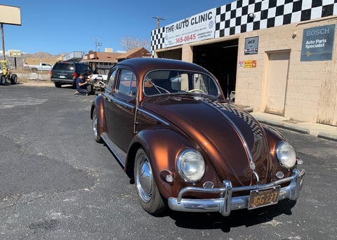 Classic copper-colored Volkswagen Beetle parked outside an auto clinic garage under clear blue sky