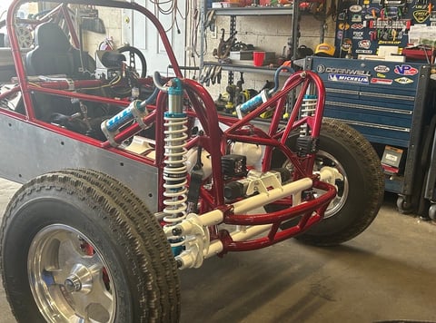 Custom red tube frame race car chassis with suspension and wide tires in workshop garage with tools