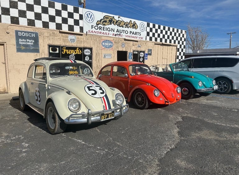 Three vintage Volkswagen Beetles parked in front of a foreign auto parts shop with checkered signage